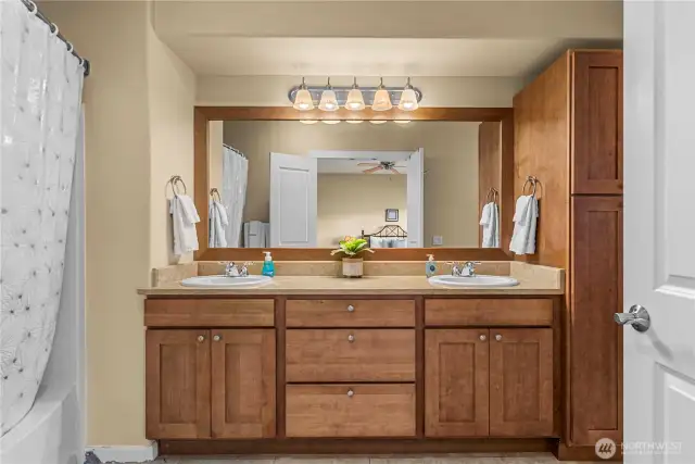 En suite bath featuring dual sinks, wood cabinetry, and shower/tub combo
