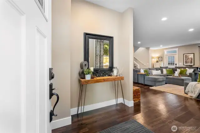 Step inside the main floor unit A with 3708sqft to enjoy where you’ll find wide plank luxury vinyl floors that check every box, waterproof, stylish, and built for real life. The rich dark tones play perfectly against warm wall colors and crisp white baseboards that stretch tall under soaring 10-foot ceilings. With the living room in view and every finish feeling intentional, this entry makes a strong first impression. This view captures what thoughtful design looks like with natural light pouring in through oversized living room windows, and a perfectly placed powder room just steps from the front door. The balance of function and style starts right at the entry and carries through every corner of the home.