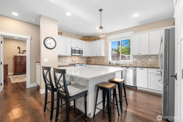 The heart of the home delivers here. A wraparound quartz island offers space for seating, serving, or just spreading out. White shaker cabinets pair with glass tile for a kitchen that feels polished. With stainless appliances included and a sink-side window for a little daydreaming, this space is as practical as it is pretty. And yes, that’s the primary suite just a few steps away.