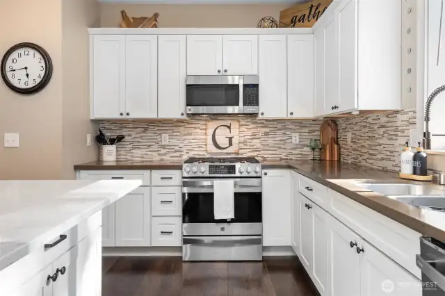 This angle gives you the full two-tone moment. Crisp white quartz on the island meets warm mushroom-colored counters along the perimeter, striking that perfect balance between modern and inviting. The gas range is ready for real cooking, and the undermount sink with a commercial-style pull-down faucet means cleanup feels just as pro. Even the microwave gets its moment, seamlessly built into the vent combo above.