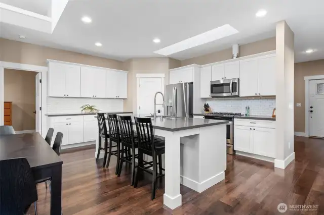 Unit B is on the main floor level as well and has 2400sqft of living space. The kitchen impresses with a large quartz island, white cabinetry, and classic subway tile backsplash. Skylights flood the space with natural light, while rich wood-tone vinyl plank floors keep it waterproof and stylish. Stainless appliances, a corner pantry, and a long beverage or baking counter complete this 9-foot ceiling beauty.
