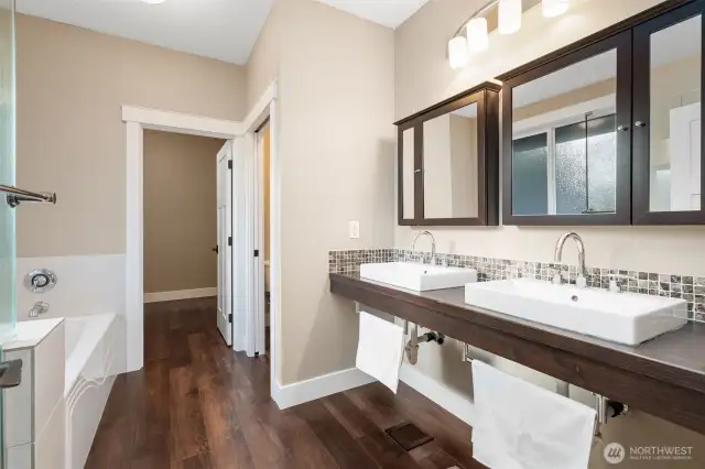 Unit B’s primary bath offers a chic blend of clean lines and smart design, featuring a suspended double sink vanity with matching medicine cabinet mirrors that add both style and storage. Relax in the deep soaking tub or refresh in the glass surround shower while soaking up the natural light. The walk-in closet is right there, ready for your wardrobe, and the stacked washer and dryer just off the entry make laundry days a breeze, tucked away but always within reach.