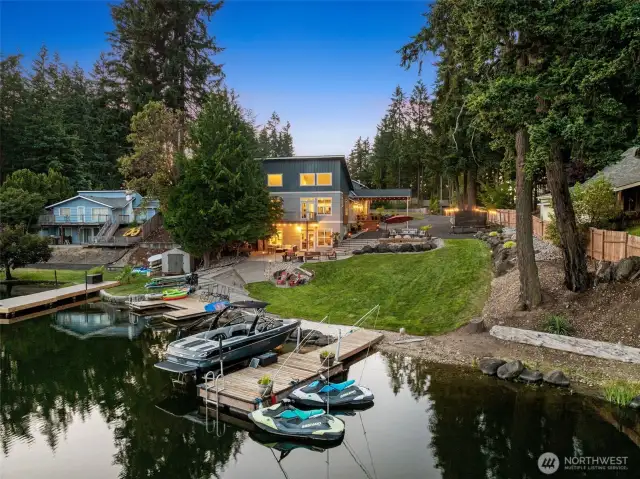 From the lake, the layout tells its story loud and clear. Two private docks extend into the water, complete with mooring whips so your boat stays safe and scuff-free. The shoreline gives way to a flat beachy area, then a gently sloping lawn that leads straight up to the fire pit, upper deck, and the separate entrance for the lower-level Airbnb. It’s the kind of setup that feels like a resort, functions like a compound, and earns like a smart investment.