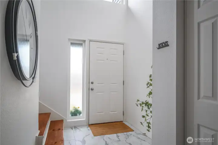 The stairs to the second level are located just off the light-filled entryway, framed by vaulted ceilings and expansive windows.