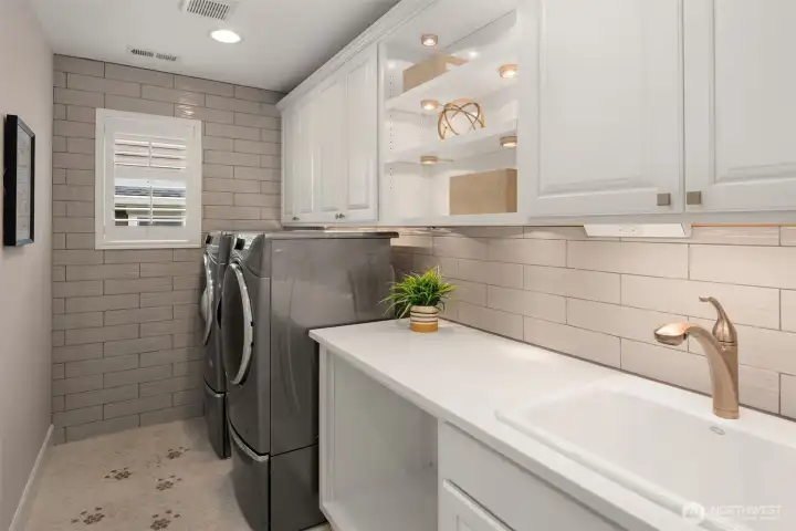 Spacious laundry with fully tiled backsplash and side wall, lighted cabinets, utility sink and extra storage!