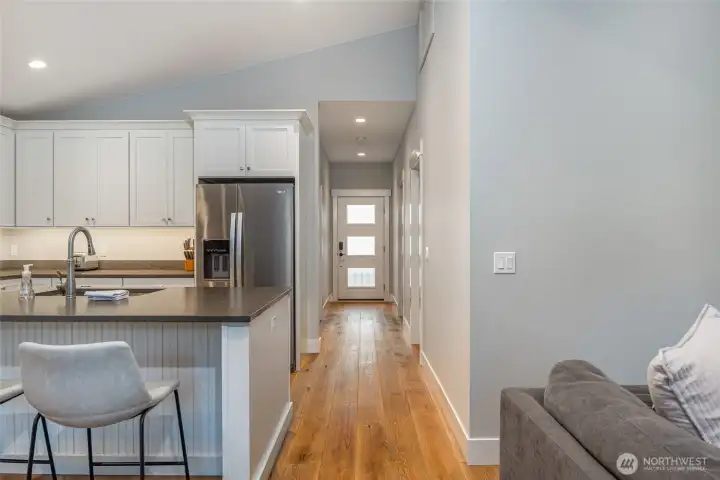 Functional layout connects kitchen to the main entry and hallway, featuring wide plank wood flooring and clean modern finishes throughout.