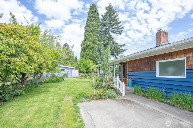 The front entry offers a lovely view of the well-manicured yard, highlighted by a mature row of rhododendrons poised to bloom and showcase their vibrant beauty.