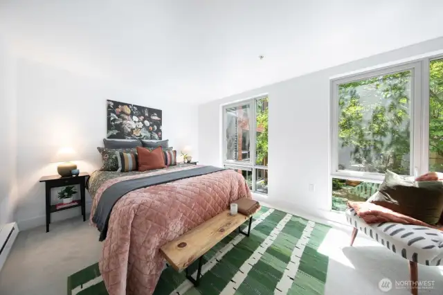 Peaceful primary bedroom with large windows and lush courtyard views.