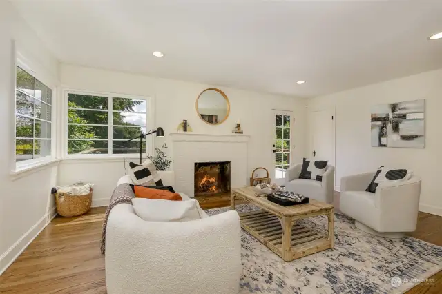 Here we are in the large living room with wood burning fireplace, and original oak hardwood floors throughout. Natural light fills this home through large corner windows on each corner of the house! The glass door to the 300 sq ft deck is to the right of the fireplace.