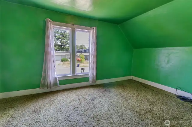 Upstairs bedroom with charming pitched ceilings and a large window that fills the space with natural light—full of potential and personality.