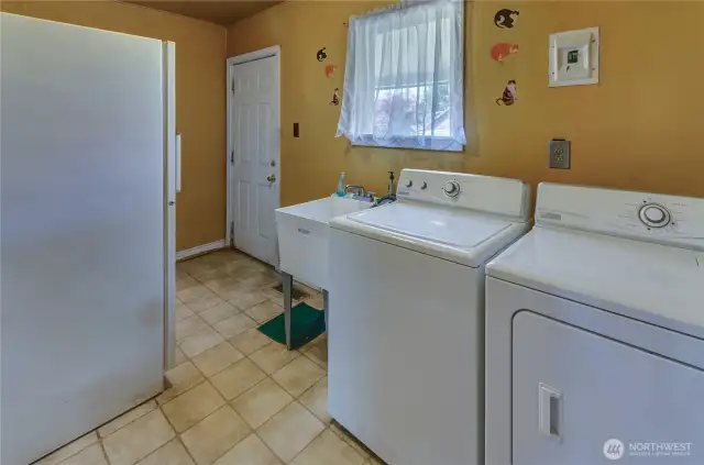 Spacious utility room with laundry, deep sink, and extra storage—conveniently located with access to the backyard.