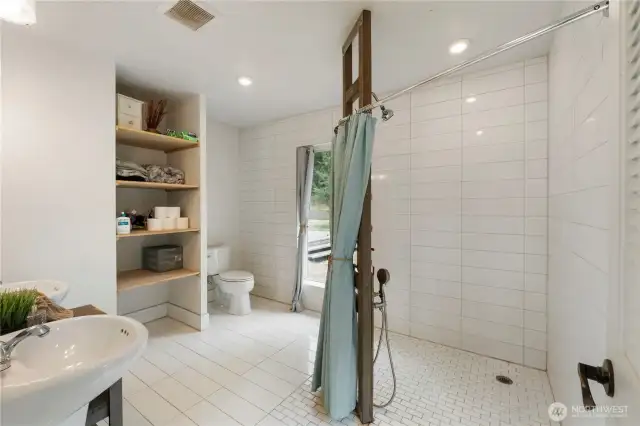 Beautiful artisan-style primary bathroom featuring a spacious walk-in shower with custom tilework and dual pedestal sinks. Thoughtfully designed with natural textures and modern lighting for a clean, spa-like retreat