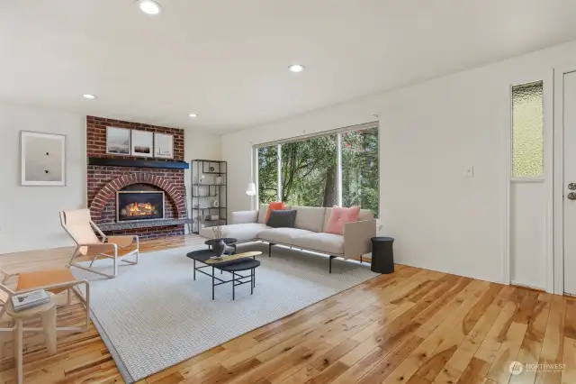 Formal living room with a gas fireplace, hardwood floors and recessed lights.  Opens to dining room.  Virtually staged photo.