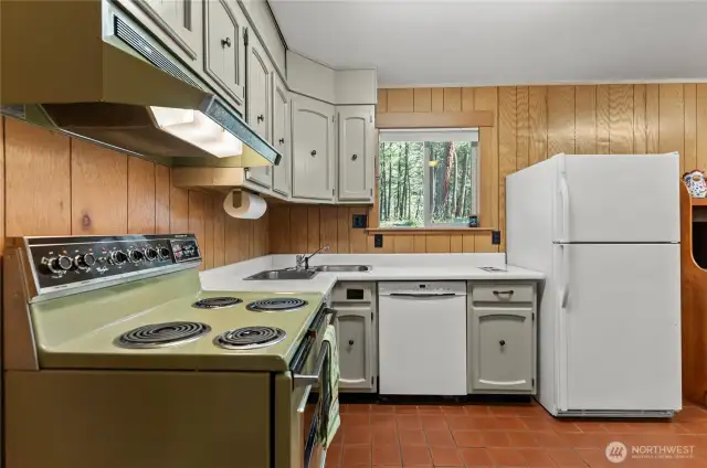Charming retro kitchen with vintage appliances, painted cabinetry, and original wood paneling—full of character and ready for your updates. Window above the sink frames a sweet view of the back yard.