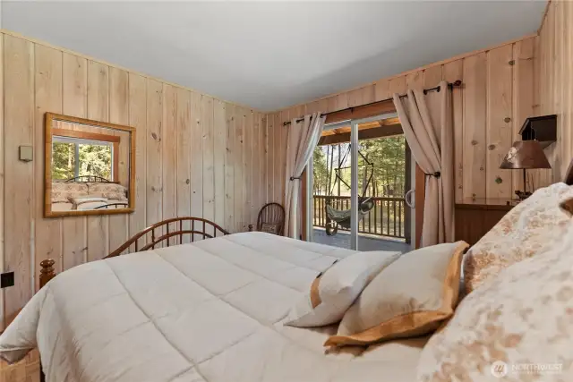 Main Bedroom with Deck Access  Wake up to filtered sunlight and river views. This cozy bedroom features pine-paneled walls and a sliding glass door that opens directly onto the deck—perfect for morning coffee or a quiet sunset unwind.