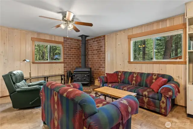 Inviting living room featuring a cozy woodstove on a classic brick hearth, warm parquet flooring, and a comfortable, open layout—perfect for relaxing or gathering with friends and family.