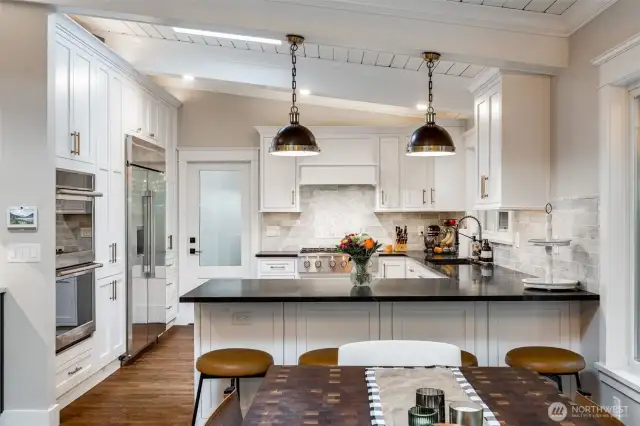 The kitchen is a culinary showpiece featuring premium soapstone surfaces, convenient dual dishwashers, an elegant Carrara marble wet bar with dedicated prep sink and professional-grade appliances including a generous 48” built-in refrigerator.