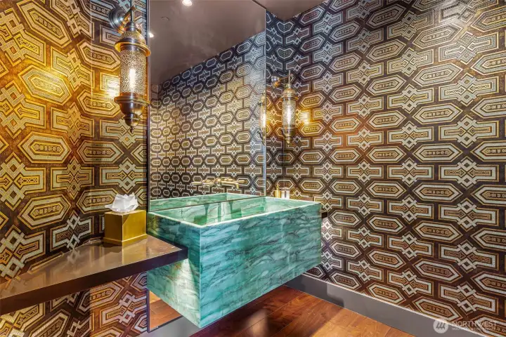 Guest will love the De Gournay hand pressed wallpaper around this emerald quartzite basin with Henry wall-mounted faucet by Waterworks. Underlit brass wrapped countertop. Moroccan-style brass light fixtures.