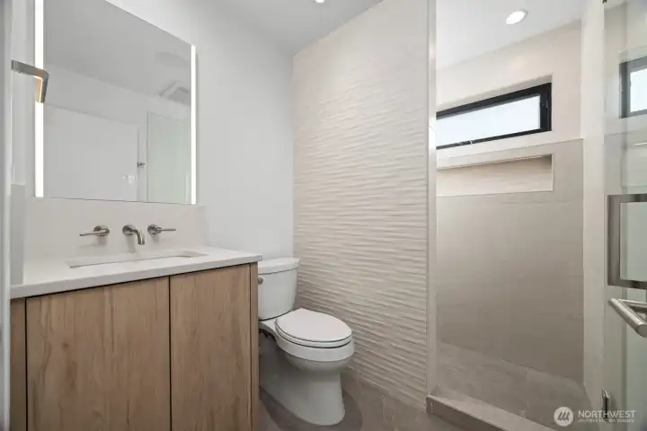 The 3/4 bath on the main floor has incredible tile work in the shower and on the wall beside the toilet. The cabinets and quartz counters match those in the kitchen.