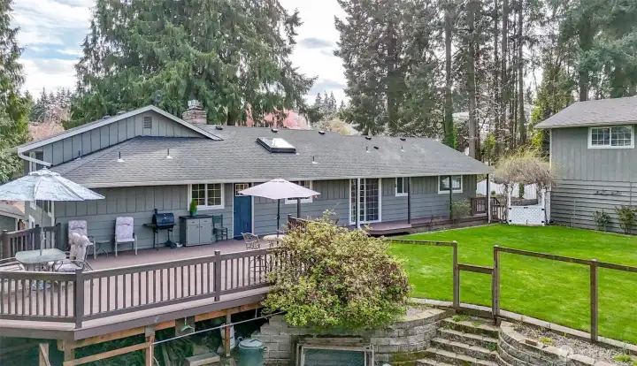 The back of the house opens to a lush mature landscape, a beautiful very spacious deck extends from the rear, providing the perfect spot for lounging, dining, and entertaining guests against a backdrop of flowering shrubs and trees.
