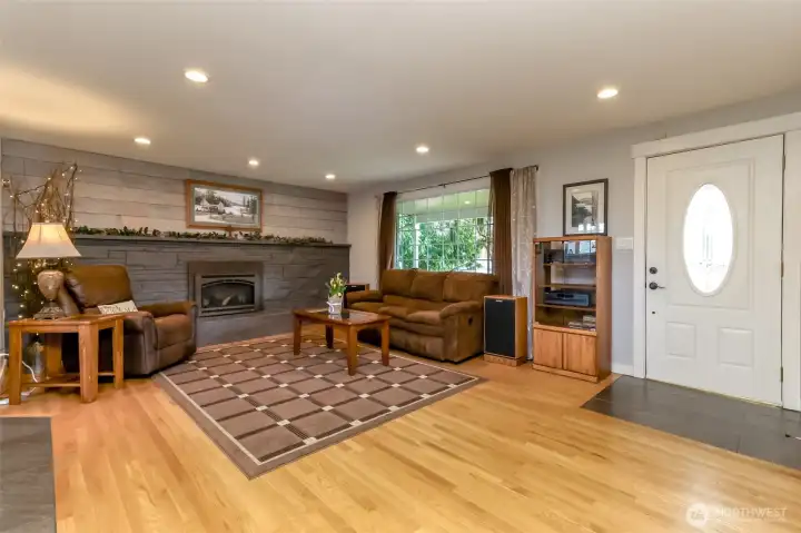 As soon as you step through the door, warmth greets you from the gleaming hardwood floors. The centerpiece is the full wall gas fireplace. A flood of natural light streams in brightening the space and highlighting the rich tone of the wood and stone. The open concept layout seamlessly connects living areas, creating an airy, welcoming flow that makes the home feel instantly inviting.