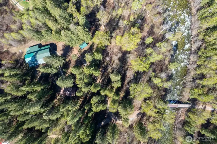 Looking down on the property - the barn and bunkhouse have green metal roofs and the brown roof of the home can be seen tucked into the trees.
