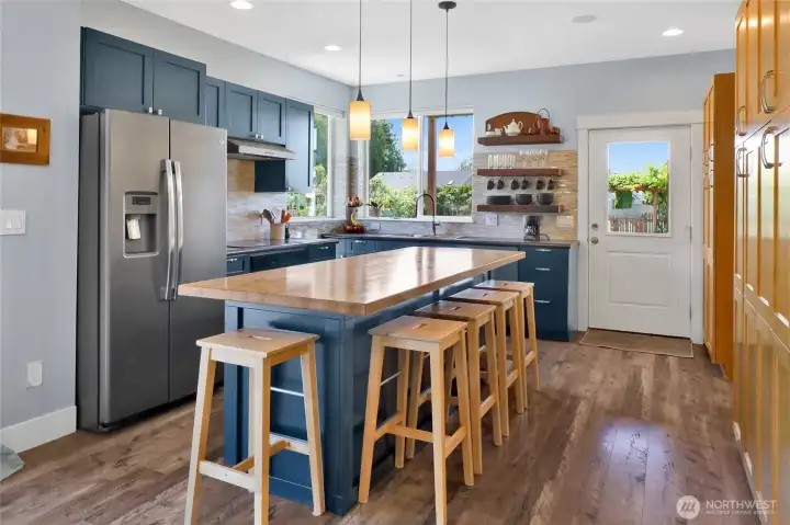 The thoughtfully designed kitchen pairs rich deep-blue cabinetry with soft blue-gray tones and natural wood accents for a warm, modern aesthetic. A spacious butcher block island and reclaimed wood open shelving above the dishwasher blend beauty with everyday functionality.