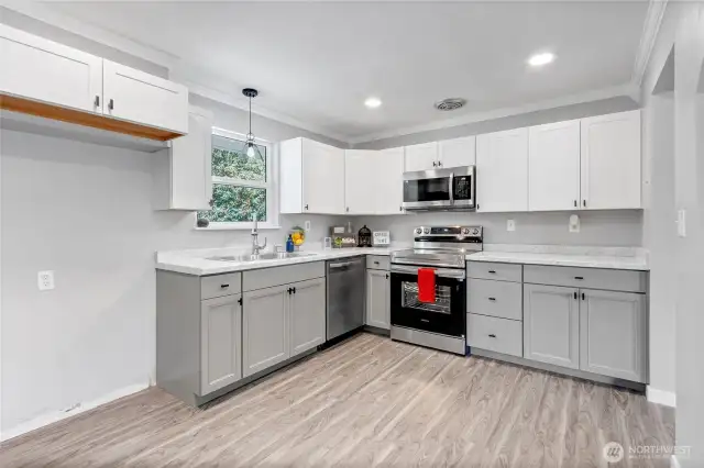 A clean, modern kitchen layout featuring a full suite of stainless steel appliances, under-cabinet lighting, and plenty of storage. The mix of white uppers and gray lowers gives a designer finish.