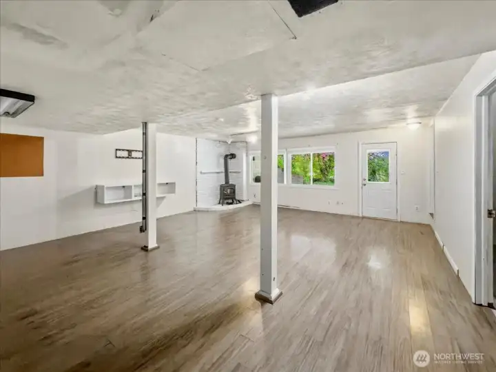 Lower level with a separate entrance and free-standing gas fireplace, offering strong potential for a private living area. To the left, you’ll find a spacious laundry room with a utility sink and direct access to the attached garage. Along the back are a convenient powder room and a large storage area.