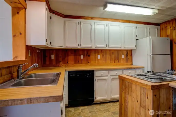Spacious kitchen featuring tons of cabinetry, cooking island, dishwasher, oven, fridge, disposal and knotty pine finishes.