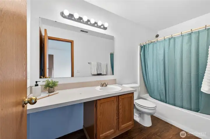 The primary bathroom features laminate wood floor and ample cabinet and counter space.