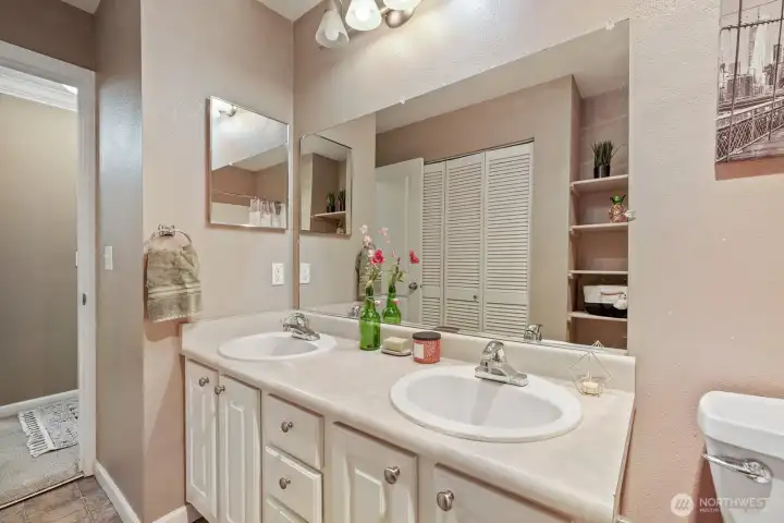 Full bathroom offers double vanity, large wall mirror, built-in shelving for linen needs. Behind the slatted bifold doors, is the full sized washer & dryer