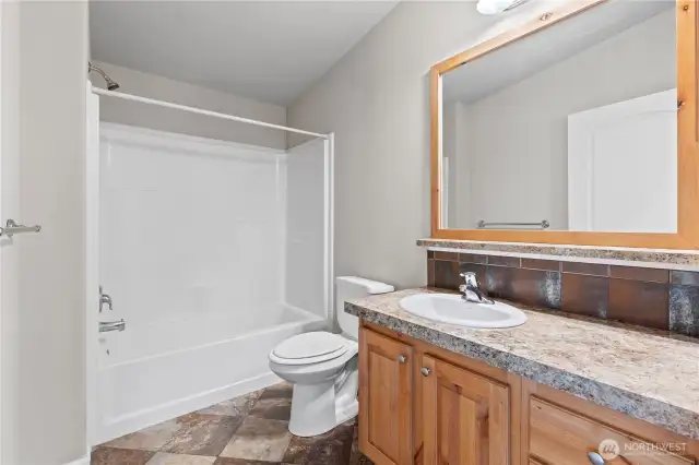 Immaculate full guest bathroom featuring a shower/tub combo, custom wood vanity, and elegant tile backsplash. This stylish and functional space is one of the many quality upgrades found in this 4-bedroom Energy Star Certified home in Lacey’s 55+ Lakeview Meadows community.