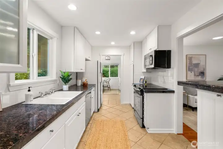 The gracious kitchen offers a breakfast bar, quartz counters, wood cabinets, a tile floor, and a garden-view window