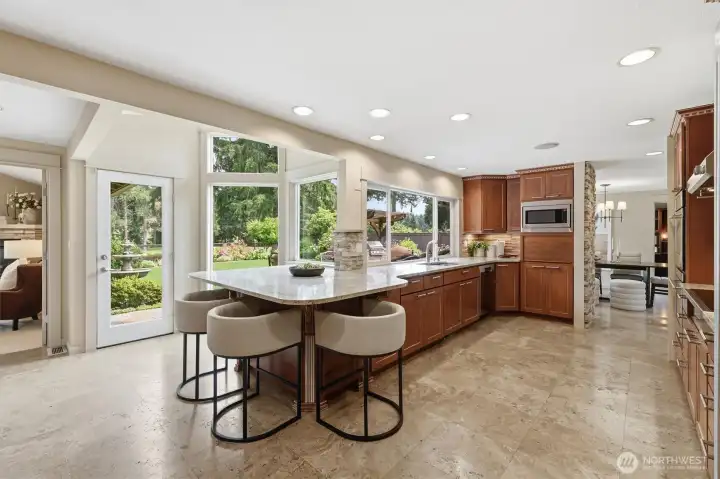 The granite-topped breakfast bar extends into a windowed nook with garden views, patio door, & vaulted ceiling.