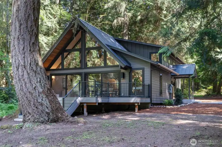 A quintessential Northwest A-frame retreat, exquisitely remodeled and set within more than nine acres of private forestland across four legal lots. Thoughtfully reimagined throughout, this extraordinary residence blends iconic architectural character with refined modern living in a serene, retreat-like setting.    The heart of the home is an expansive open-concept kitchen anchored by an enormous island, designed for effortless entertaining and everyday gathering. A dramatic wall of sliding doors opens seamlessly onto an expansive deck overlooking the sprawling front lawn and surrounding forest, creating a stunning indoor-outdoor living experience immersed in nature.    The main level offers exceptional flexibility with a spacious media room, two bedrooms, and a full bathroom. Upstairs, the private primary suite features a spa-inspired ensuite bath and oversized walk-in closet. A lofted bonus space is ideal for a home office, fitness studio, yoga retreat or meditation lounge.