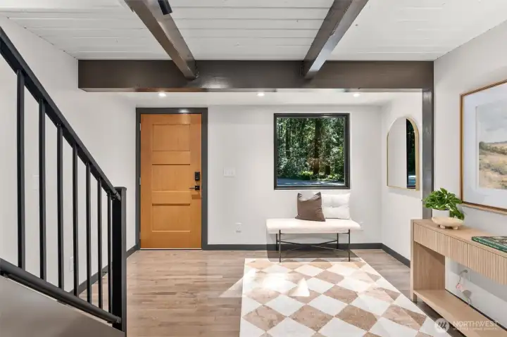 First impressions are everything, and this sophisticated foyer sets a breathtaking tone for the entire home. Step through the warm wood front door onto gleaming, classic hardwood floors that guide you into the heart of the residence. Bold architectural beams and clean planked ceilings echo the home's contemporary design, while a large picture window frames a vibrant view of the private woods outside—acting as a living piece of art. Spacious, open, and filled with natural light, this entry offers an immediate sense of calm and style the second you arrive.