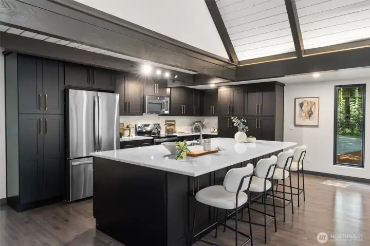 The impeccably designed kitchen is a chef's dream, boasting an abundance of sleek cabinetry, subtle under-cabinet task lighting, and premium matching stainless steel appliances. Expansive white quartz countertops provide endless prep space and wrap into a massive island perfect for casual dining. With fluid transition from the kitchen to the main living area, this light-filled home is an absolute masterpiece for both entertaining and luxurious daily living.