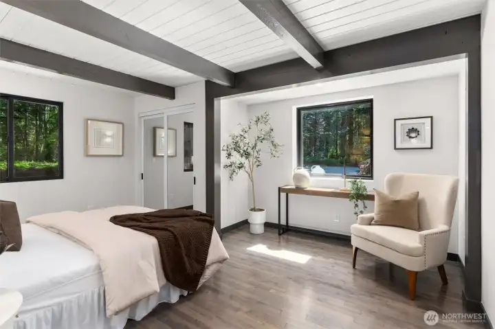 Wake up surrounded by the peaceful beauty of nature in this generously oversized main-floor bedroom. Crisp white walls and bold architectural ceiling beams create a sophisticated, airy backdrop, while two large windows perfectly frame the lush, serene views outside. The true luxury of this space is its versatility—featuring a spacious, dedicated alcove ideal for a quiet home office, reading study, or morning meditation nook. It’s more than just a bedroom; it’s a self-contained retreat designed for ultimate relaxation.