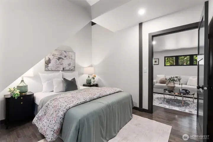 Tucked away on the upper level, this impressive fourth bedroom is a complete self-contained retreat. Dramatic, sharply angled cathedral ceilings lined with clean white planking and anchored by bold dark beams give the room an airy, sophisticated vibe. Large windows bring the tranquil forest views right to the bedside. Perfect for guests, older children, or a second primary setup, this room offers the ultimate privacy with its own dedicated walk-in closet and a gorgeous attached ensuite bathroom featuring a modern vanity and premium finishes.