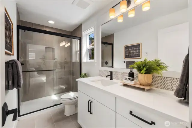 Large lower level bathroom, with a shower and white and grey marble-look quartz countertops.