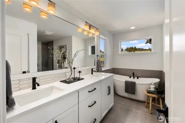 Large primary bathroom with large-scale tiled floors, a soaking tub, shower with frameless glass and dual sinks with white and grey marble-look quartz countertops.