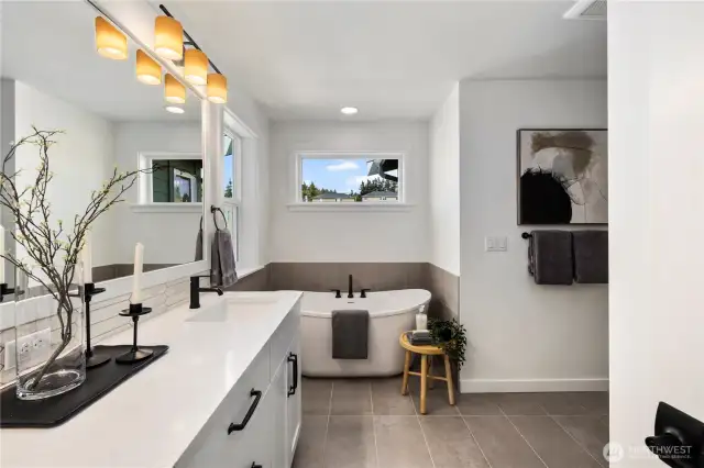 Large primary bathroom with large-scale tiled floors, a soaking tub, shower with frameless glass and dual sinks with white and grey marble-look quartz countertops.