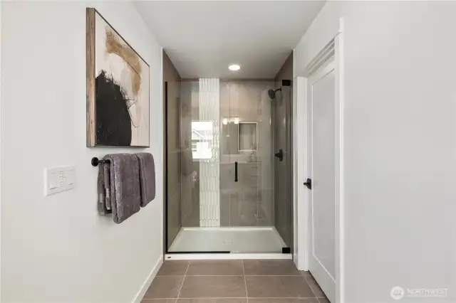Large primary bathroom with large-scale tiled floors, a soaking tub, shower with frameless glass and dual sinks with white and grey marble-look quartz countertops.