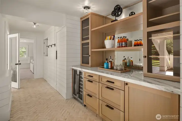 Lower-level refreshment area featuring custom millwork, beverage fridge, and access to the outdoors.