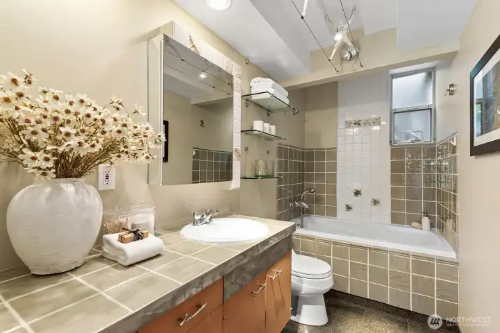 Well-appointed bathroom featuring tiled surfaces, ample counter space, and a full tub
