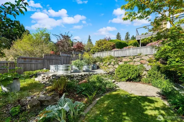 Lush, terraced garden with raised beds and mature landscaping creates a private, park-like setting—perfect for gardening enthusiasts and outdoor enjoyment
