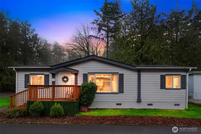 Charming curb appeal with a welcoming front porch and lush greenery set against a backdrop of tall evergreens.