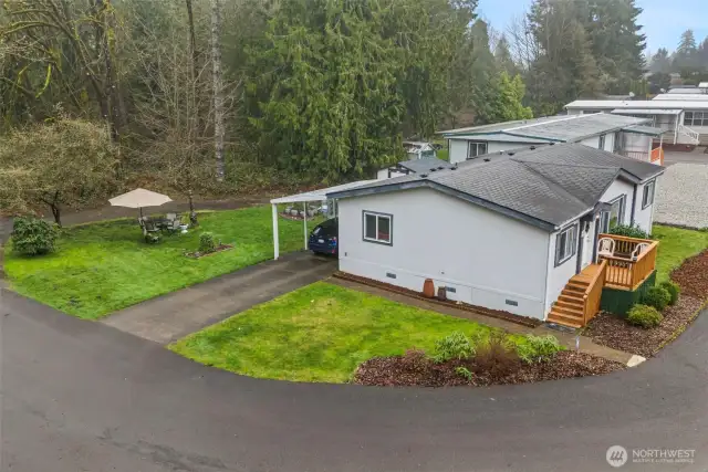 Peek at the lush yard and extra parking — including a covered carport — with mature landscaping, tall pines, and serene tree-lined views.