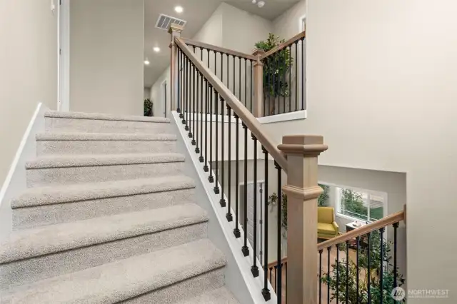 Upstairs retreat begins with this beautifully crafted staircase featuring plush carpeting, wood accents, and iron balusters—offering a warm welcome to the private living spaces above.